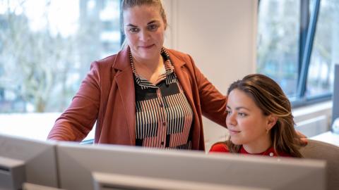 Liesbeth van Kerkwijk geeft instructies aan een collega achter een computer