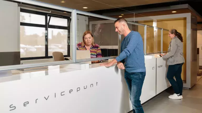 Een collega staat bij het servicepunt en is in gesprek met een andere collega