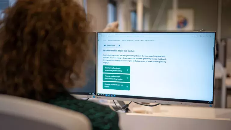 Een persoon kijkt naar een scherm waar toelichting over bezwaar maken tegen een besluit staat beschreven. 