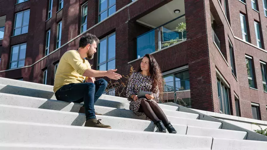 Twee collega's zittend in gesprek buiten op een trap